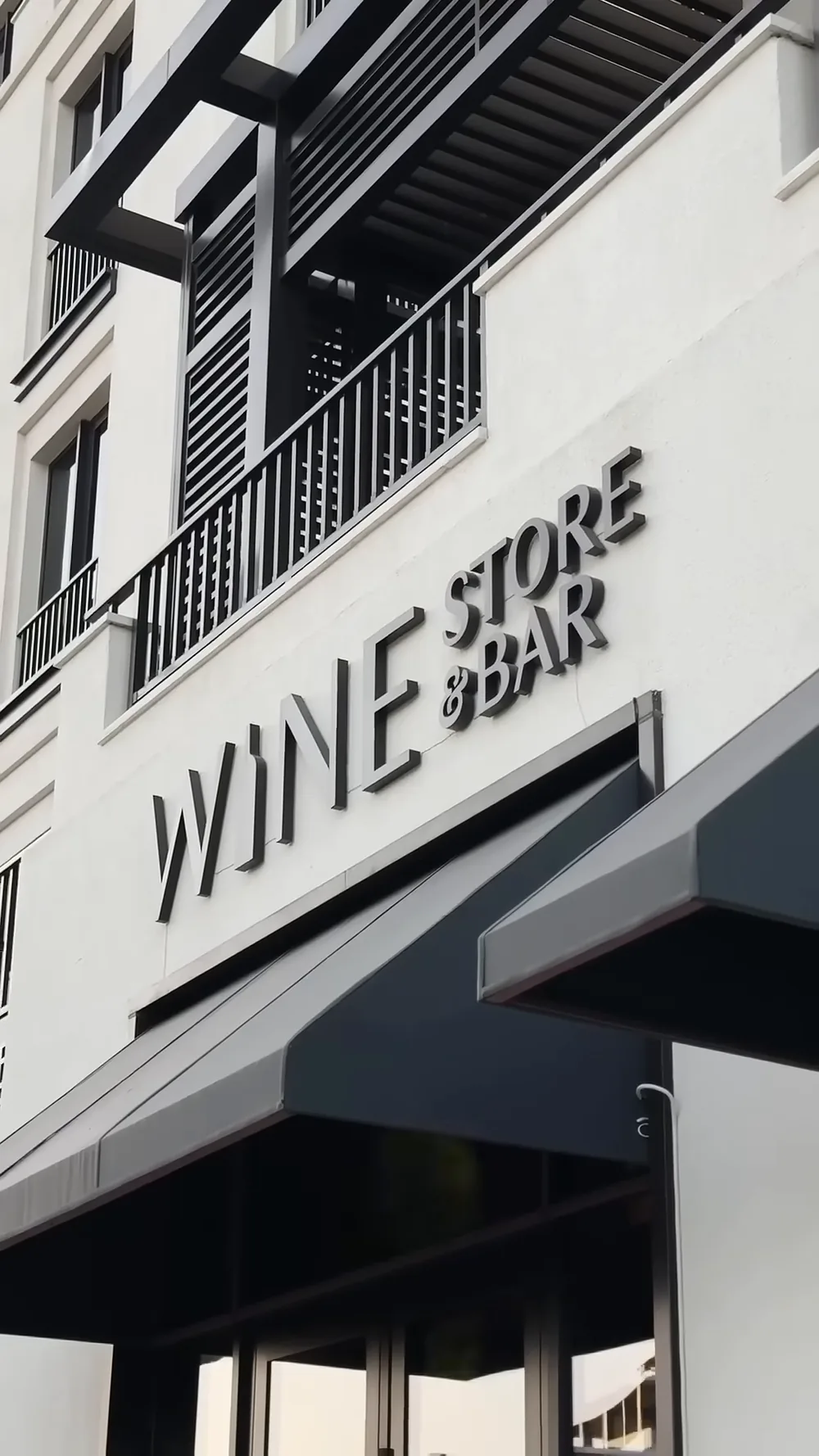 Вывеска WINE STORE & BAR над входом с графитовыми маркизами — первый этаж The Grand